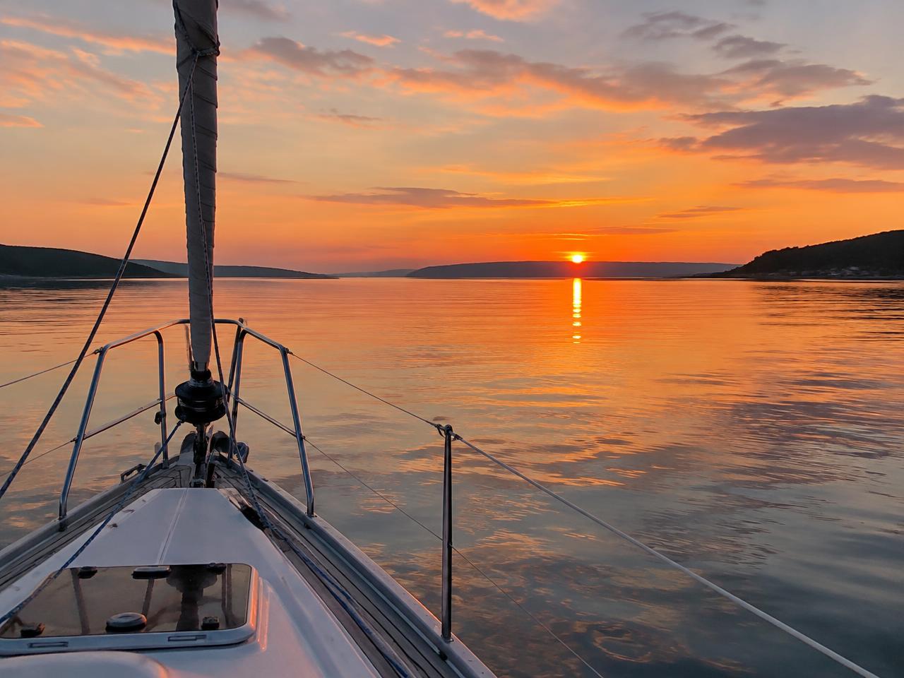 Solnedgang over en stille fjord set fra sejlbådens stævn